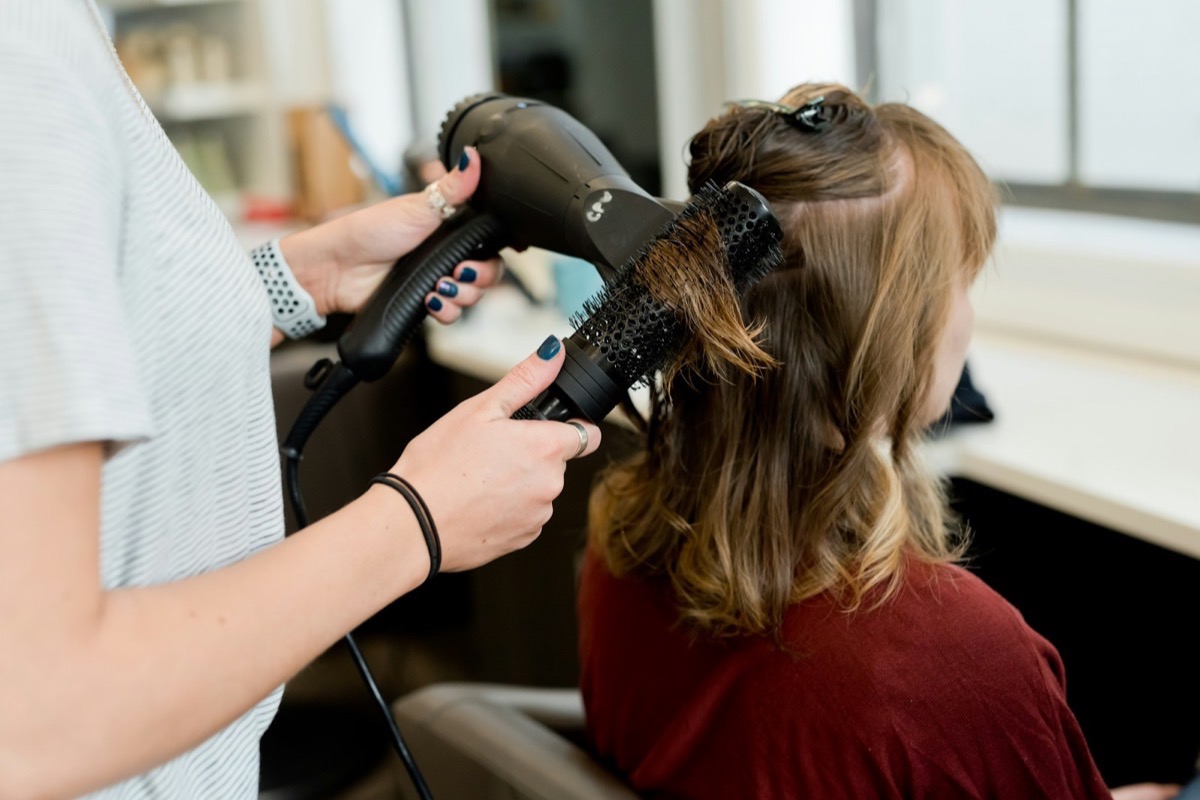 A hairstylist blow-drying a client with a round brush